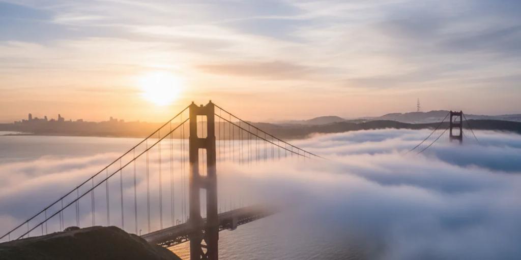 Le Golden Gate Bridge émergeant d'une brume basse au lever du soleil, ses tours couleur International Orange se détachant sur un ciel pâle